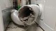 © Gophotograph - Close up view of a heavily clogged dryer vent hose filled with flammable lint and dust in a residential laundry room creating a potential fire hazard