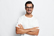© SHOTPRIME STUDIO - Smiling man wearing glasses and white t-shirt stands confidently with crossed arms against a solid background. Portrait reflecting positive vibes and casual style.