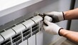 © Netsai - Close-up of gloved hands adjusting a thermostatic valve on a white home radiator to control heating.