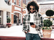 © halayalex - Handsome smiling hipster  model. Sexy unshaven Arabian man dressed in summer clothes. Fashion male with long curly hairstyle using smartphone apps, looking at cellphone screen. Holds phone