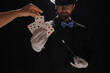 © Pixel-Shot - Male magician and female hand taking playing card on dark background