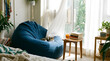 © SIMANG - A cat resting on a blue bean bag chair near a sunlit window with green plants indoors