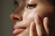 © Olga Ко - Close-up de uma jovem mulher brasileira aplicando creme hidratante no rosto, pele com sardas iluminada pelo sol, conceito de skincare e beleza natural