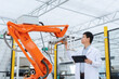 © zhu difeng - Engineer operating an orange industrial robotic arm to inspect a metal component in a factory setting