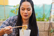 © Sabrina - Happy young asian woman eating instant noodles outdoor - Lunch break, fast food, thai culture and lifestyle concept