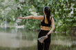 © PRIYO DWI SAPUTRO - A young asian woman practices yoga outdoors, balancing on one leg with one arms extended, surrounded greenery by the lake at morning.