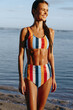 © SHOTPRIME STUDIO - Young woman in colorful striped bikini stands on the beach smiling happily with wet skin and hair enjoying sunny summer lifestyle near calm sea water.