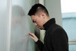 © fotolite - A defeated young Asian male student slumps forward with his head against a whiteboard filled with math equations, ideal for academic burnout, student struggle, or STEM pressure concepts.