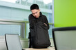 © fotolite - A young Asian male student leans over and searches through a backpack on a desk in a campus study room, ideal for student preparation, campus life, or back to school concepts.