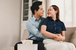 © PRIME STOCK LAB - Affectionate Asian couple embracing and smiling at each other while relaxing on a living room sofa