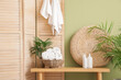 © Pixel-Shot - Folding screen, houseplants and wicker basket with clean folded towels on bench near green wall