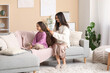 © Pixel-Shot - Young mother brushing hair of her little daughter while sitting on sofa at home
