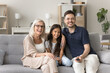 © fizkes - Older granny her little granddaughter and young adult son watching family movie seated on sofa in modern living room, laughing over comedian movie plot, enjoy recreational activity on weekend at home