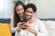 © Pormezz - Relax and happiness lifestyle at home concept. Young couple sitting on sofa in living room looking at smartphone smile on face in cozy atmosphere.