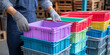 © S-DESIGN - Worker in blue apron and gloves organizes colorful plastic storage bins in a warehouse setting with wooden pallets visible in the background