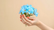 © Olena Liulko - A graceful hand with vibrant orange manicure gently cradles a delicate bouquet of bright blue flowers against a soft, neutral beige background, creating a striking and elegant color contrast