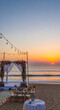 © Lucianastudio - Romantic beach wedding ceremony setup at sunset with floral decorations and string lights overlooking the ocean