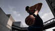 © master1305 - Man holding basketball in city street wearing headphones low angle urban sport concept. Concept of street sport culture, active lifestyle, youth energy, performance and urban training visuals.