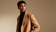© Anna - A stylish young Black man wearing a camel coat and black turtleneck. Confident male model posing for a fashion portrait in a studio with copy space