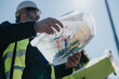 © qunica.com - Construction engineers wearing hard hats and high-visibility vests review layered site plans outdoors. The team studies blueprints and maps while coordinating on a sunny construction site.