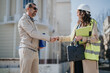© qunica.com - A construction engineer in a hard hat and hi vis vest shakes hands with a client outside a building. The two professionals greet each other during an on-site meeting and discussion.