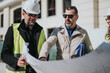 © qunica.com - Two construction professionals examine a large blueprint at an outdoor building site. They review plans together during an on-site project meeting.