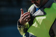 © qunica.com - A construction engineer wearing a high-visibility safety vest speaks into a walkie talkie. The worker communicates on site while checking equipment and safety gear.