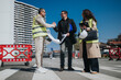 © qunica.com - Three construction professionals review blueprints and shake hands on an urban roadwork site. A client and site managers discuss plans beside safety barriers and helmets under a clear sky.