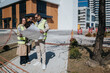 © qunica.com - Two construction professionals in safety vests examine large architectural blueprints on a paved urban site. Colleagues review plans together near a building under development in a city setting.