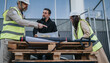 © qunica.com - Construction engineers review building plans on a temporary worktable at an outdoor site. Three professionals in hard hats and safety vests discuss blueprints during a site meeting.