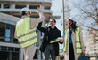© qunica.com - Construction engineers celebrate progress on a building site with a high five while holding plans.