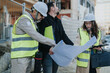 © qunica.com - Construction engineers review blueprints at an urban building site while wearing hard hats and reflective safety vests. A team of professionals studies plans and discusses project details on site.