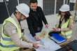 © qunica.com - Construction engineers review blueprints and site plans at an outdoor building site. A team in hard hats and high-visibility vests examines drawings and documents together.