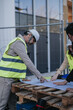 © qunica.com - Construction engineers in hard hats and reflective vests examine blueprints on a job site. They point to plans spread on a pallet while discussing the building layout.