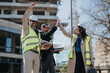 © qunica.com - Construction engineers wearing hard hats and high-visibility vests celebrate on an urban building site. Three colleagues share a victorious high five while reviewing plans and equipment.