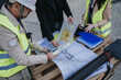 © qunica.com - Construction engineers in safety vests examine blueprints and site plans on a wooden pallet. The team reviews architectural drawings and project documents during an on-site planning meeting.