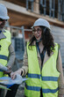 © qunica.com - A female construction engineer in a hard hat and high-visibility vest reviews plans with a colleague on a building site.