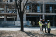 © qunica.com - Construction engineers in hard hats and safety vests review plans at an urban building site. They stand by a partially constructed concrete building while discussing blueprints.