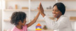 © Prostock-studio - A child and an adult are engaged in a building blocks activity inside a well-lit room. They are smiling and giving each other a high five after completing a structure. Toys are placed nearby.