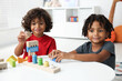 © New Africa - Cute little brothers playing with toys at white table indoors