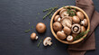 © Sana - A bowl of fresh mushrooms on a dark slate surface with herbs and a brown cloth
