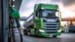 © SSP - A green fuel pump nozzle at a gas station with a large green truck blurred in the background.