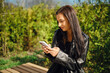 © boomeart - Woman sitting on bench texting on phone in sunny outdoor setting with greenery