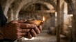 © Fatima Sial - Ancient clay oil lamp held in weathered hands, traditional terracotta lighting in stone cellar, historical middle eastern candle light