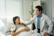 © Crystal - Young male doctor using stethoscope for a check up, listening to heartbeat of a female Asian patient lying in a hospital bed