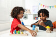 © New Africa - Cute little brothers playing with toys at white table indoors