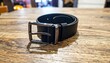 © asmara - Black Leather Belt with Silver Buckle on Wooden Table.