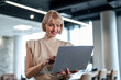 © Migma_Agency - Smiling businesswoman using laptop standing in modern office