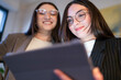 © Studio Marmellata - Two young women in business attire look at a tablet together, smiling and engaged in discussion.