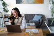 © Studio Marmellata - A young woman works on her laptop and uses a calculator while sitting at a desk in a home office.